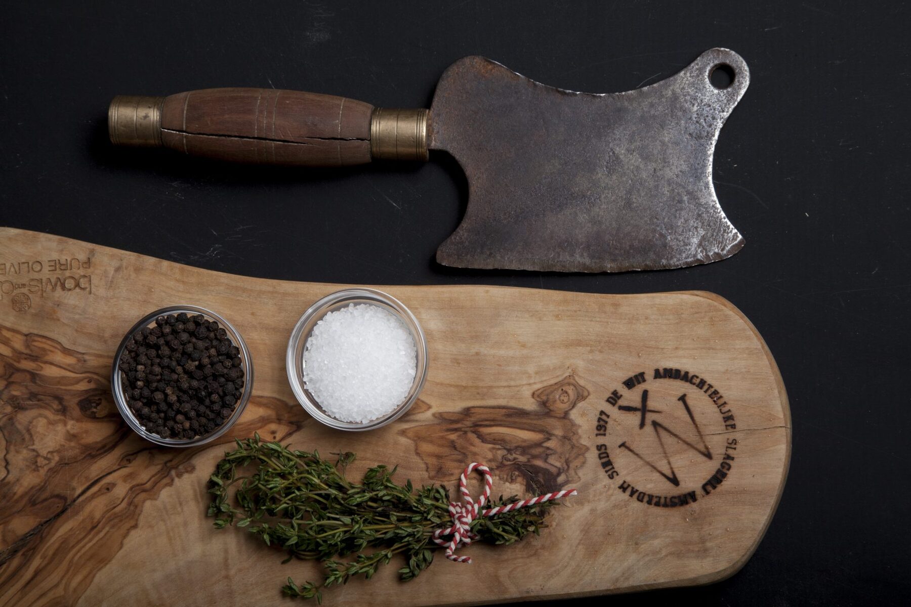 Oud hakmes op een snijplank met het logo van Slagerij de Wit, peper, zout en tijm